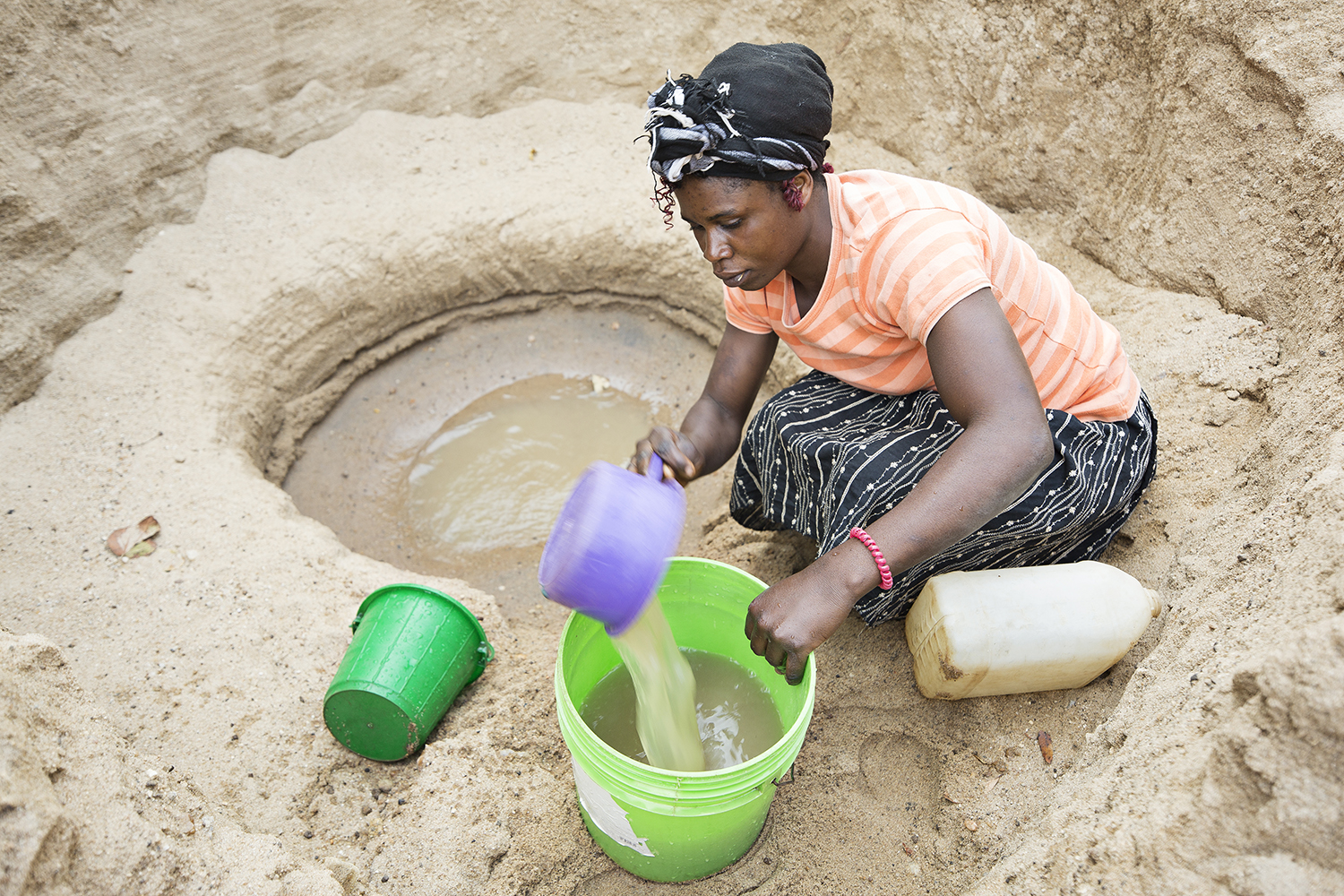 Kvinde arbejder ved et vandhul og skovler vand op